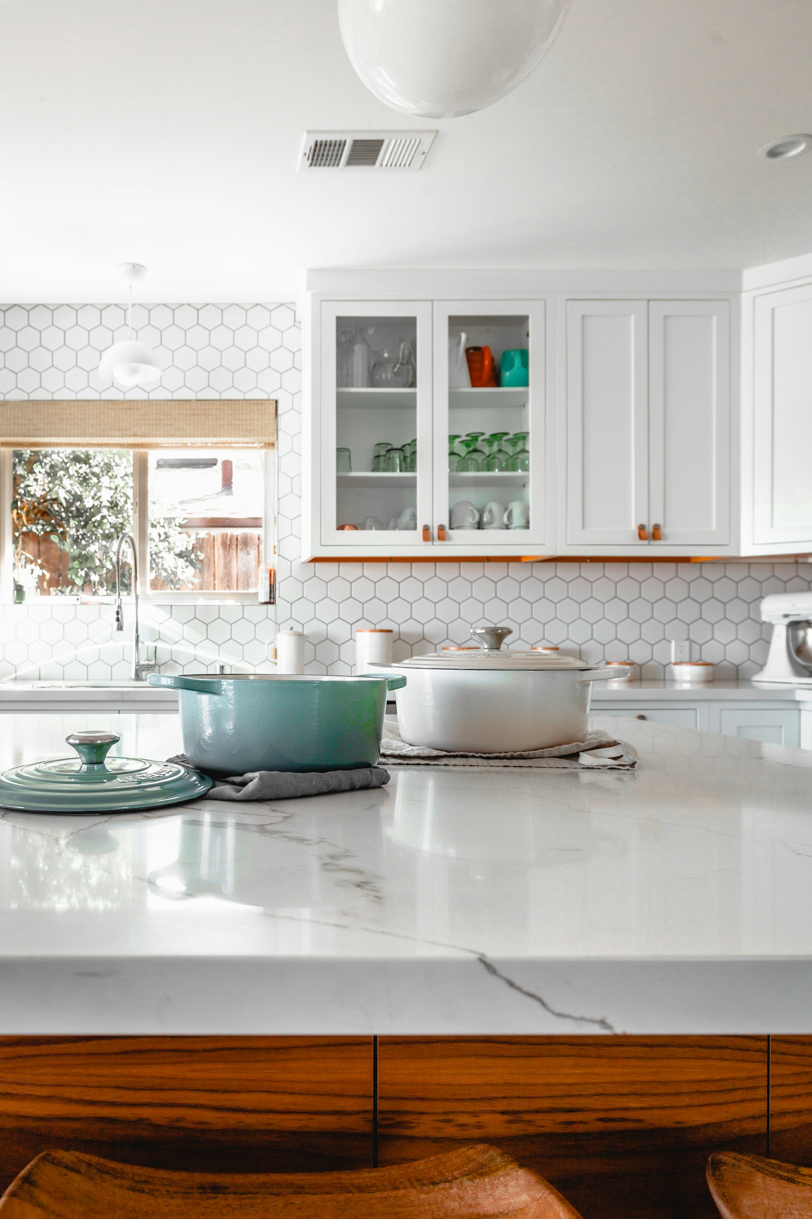 A bright kitchen with a marble island, white cabinets, and wood drawers